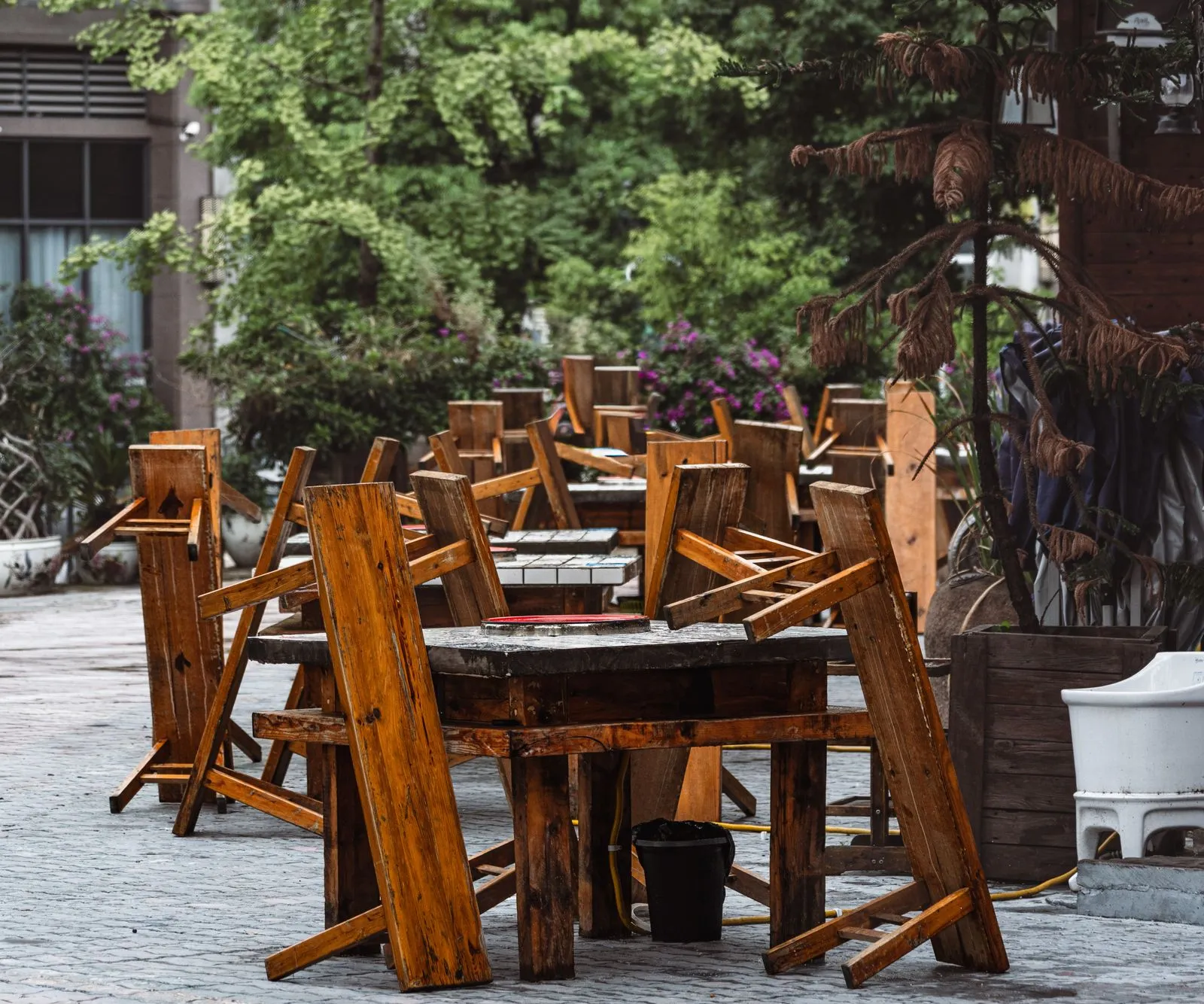 Rustic outdoor cafe setting with wooden tables and chairs arranged upside down.